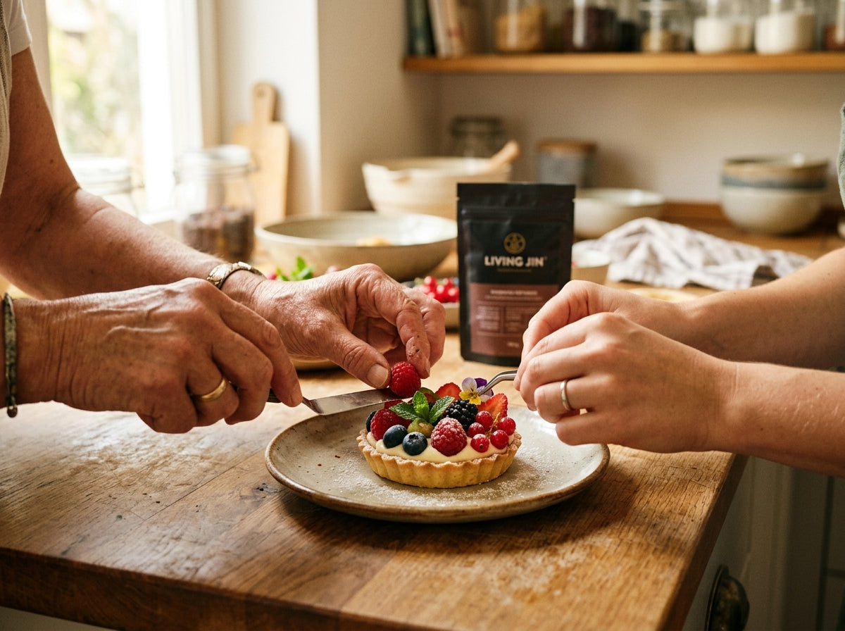 Two pairs of hands collaboratively plating a healthy fruit tartlet in a sunlit kitchen, representing the warm Living Jin culinary community.