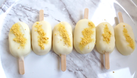 Row of ice cream popsicles with yellow toppings on a marble surface