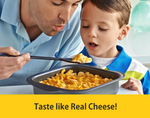 A heartwarming lifestyle image of a father blowing on a spoonful of creamy macaroni and cheese to cool it down for his young son. They are both looking eagerly at the dish in a black baking pan. A bold yellow banner at the bottom reads "Taste like Real Cheese!", promoting Living Jin's dairy-free Magic Cheese powder as a delicious, family-friendly plant-based alternative.